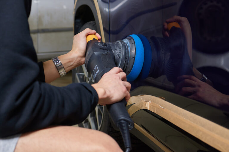 Man with an orbital polisher in car workshop polishing car closeup